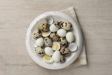 Unpeeled and peeled hard boiled quail eggs in bowl on white wooden table, top view
