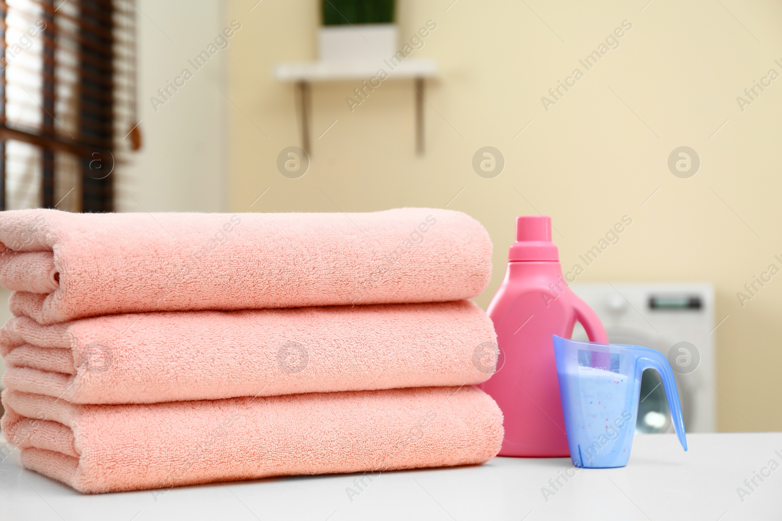 Photo of Stack of clean towels and detergents on table in laundry room