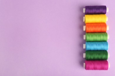 Photo of Different colorful sewing threads on lilac background, flat lay. Space for text