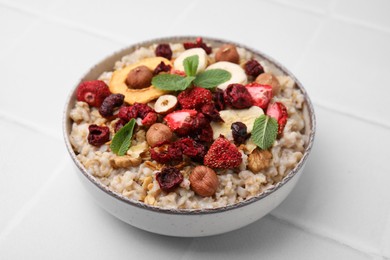 Photo of Oatmeal with freeze dried fruits, nuts and mint on white tiled table, closeup