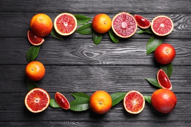 Photo of Frame of whole and cut red oranges on black wooden table, flat lay. Space for text
