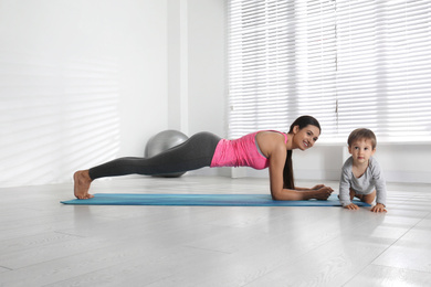 Young woman doing exercise with her son indoors. Home fitness