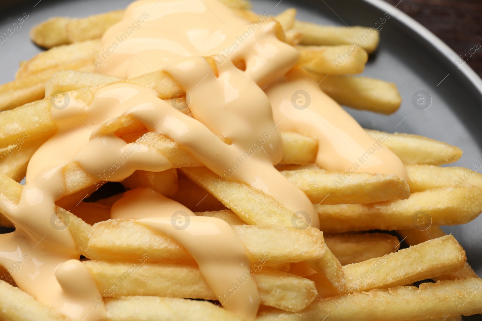 Photo of Delicious french fries with cheese sauce on plate, closeup