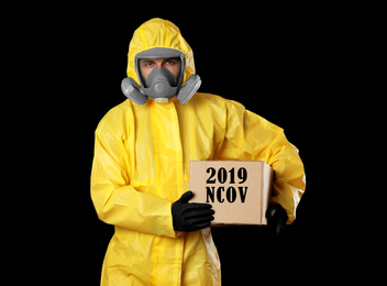 Man wearing chemical protective suit with cardboard box on black background. Coronavirus outbreak