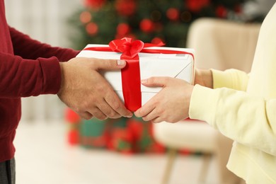 Photo of Man giving woman Christmas gift box received by mail indoors, closeup