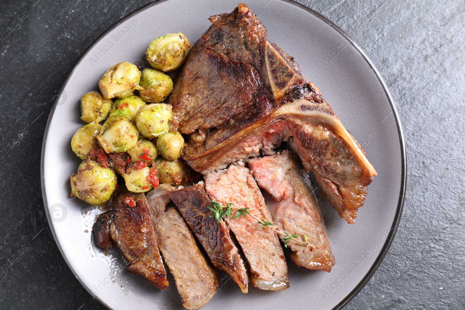 Photo of Delicious fried beef meat, vegetables and thyme on black table, top view