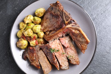 Delicious fried beef meat, vegetables and thyme on black table, top view