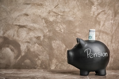 Photo of Black piggy bank with word PENSION and money on table