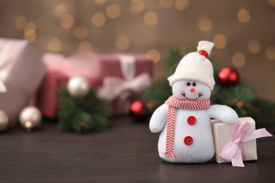 Photo of Snowman toy and Christmas box on table against blurred festive lights. Space for text