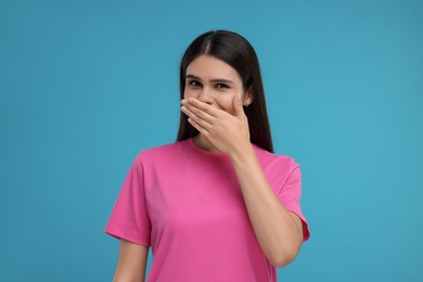 Embarrassed woman covering mouth with hand on light blue background
