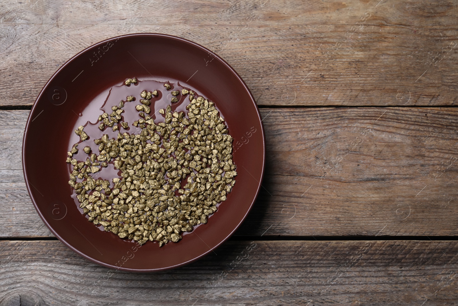 Photo of Plate of gold nuggets on wooden table, top view. Space for text