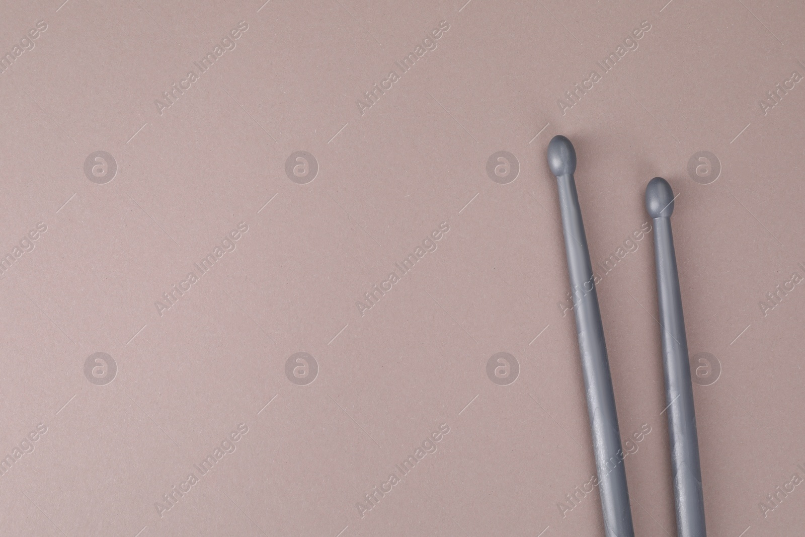 Photo of Two gray drum sticks on dusty rose background, top view. Space for text