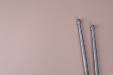 Photo of Two gray drum sticks on dusty rose background, top view. Space for text