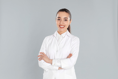 Photo of Happy young woman in lab coat on light grey background