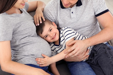 Photo of Pregnant mother, father and son spending time together on sofa at home. Family time