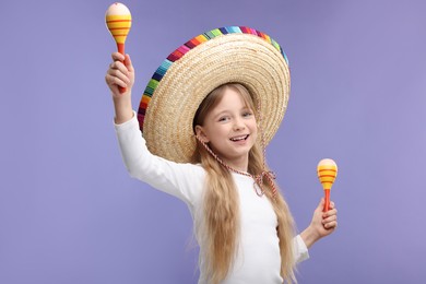 Photo of Cute girl in Mexican sombrero hat dancing with maracas on purple background