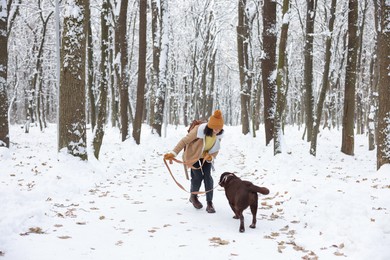 Photo of Woman walking with adorable Labrador Retriever dog in snowy park