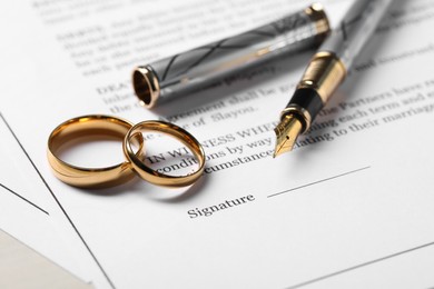 Marriage contracts, gold rings and pen on light wooden table, closeup