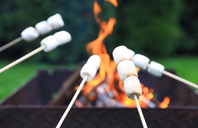 Photo of Delicious puffy marshmallows roasting over bonfire, closeup