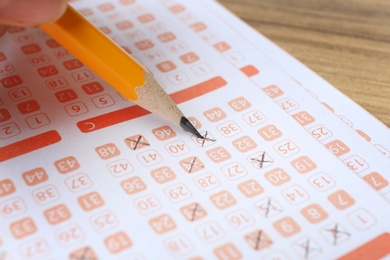 Photo of Woman filling out lottery tickets with pencil on wooden table, closeup. Space for text