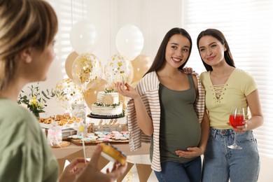 Photo of Happy pregnant woman and her friends with tasty treats at baby shower party