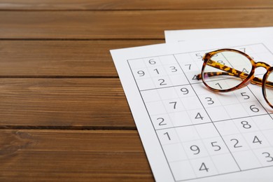 Sudoku and eyeglasses on wooden table, space for text