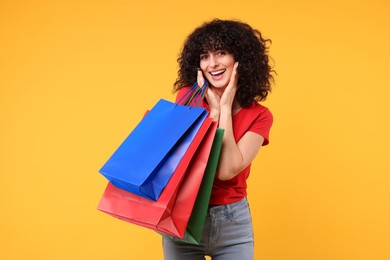 Happy young woman with shopping bags on yellow background