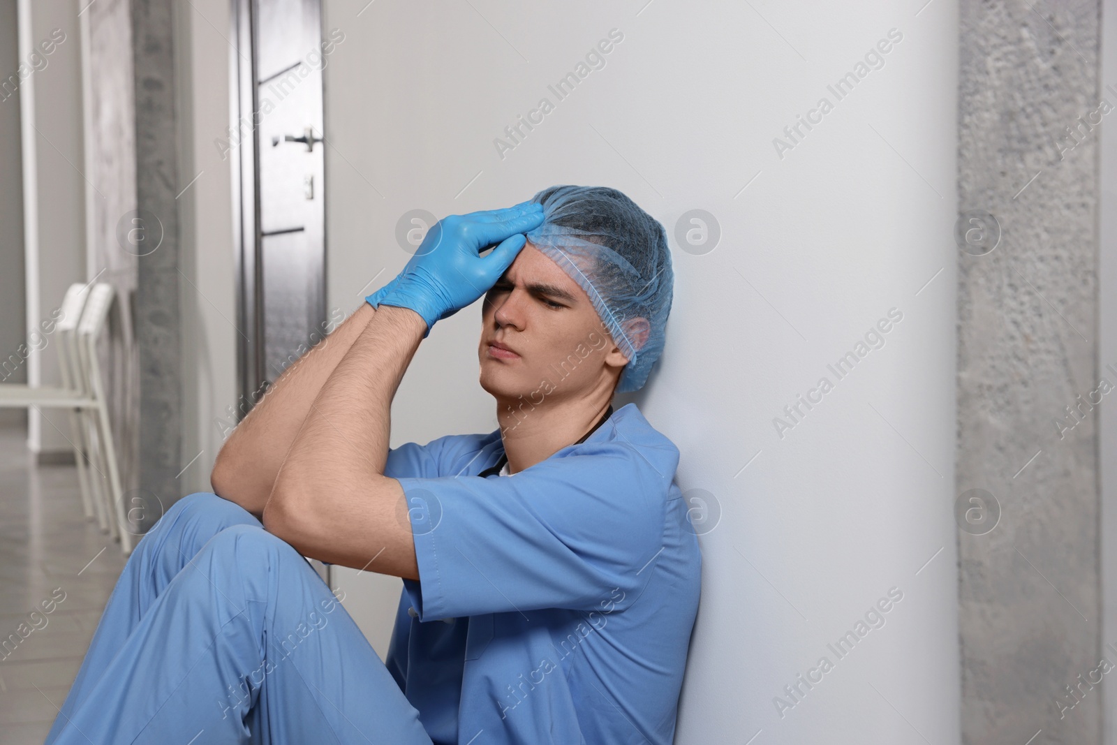 Photo of Exhausted doctor sitting near grey wall in hospital hallway