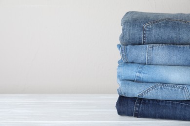Photo of Stack of different jeans on white wooden table. Space for text