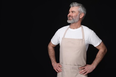 Photo of Happy man wearing kitchen apron on black background. Mockup for design