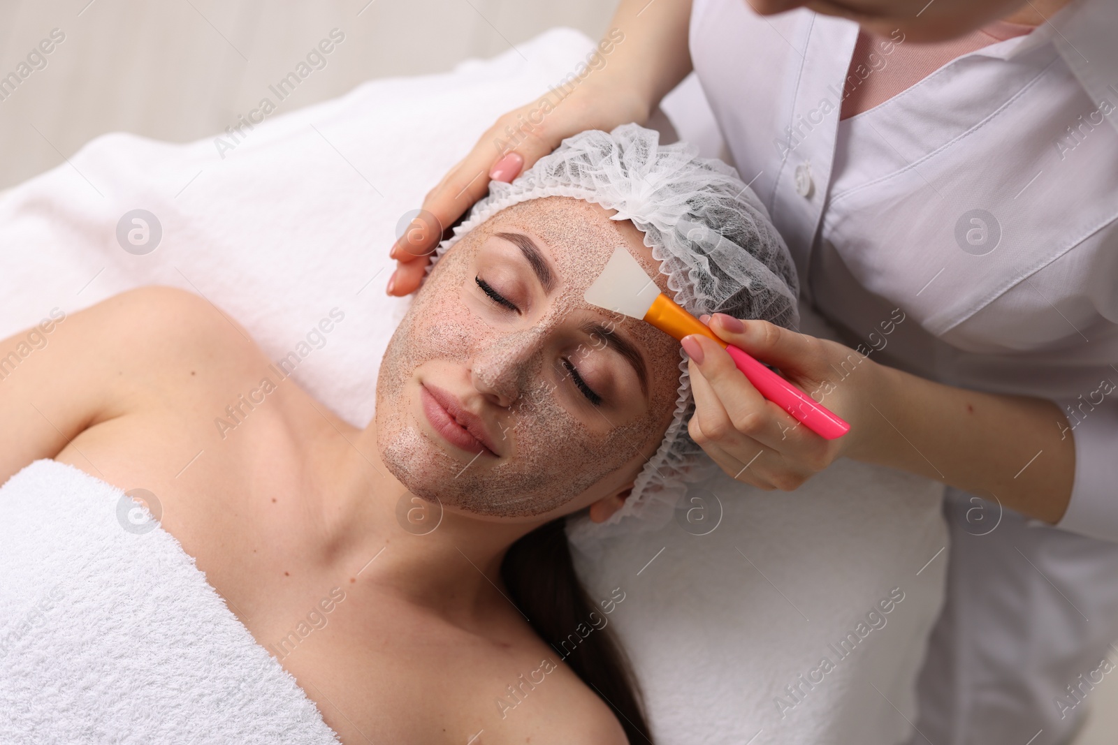 Photo of Cosmetologist applying mask on woman's face in clinic, top view