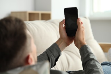 Photo of Man laying on sofa and using smartphone at home, closeup