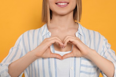 Photo of Young woman making heart with hands on yellow background, closeup. Volunteer concept