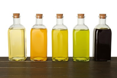 Photo of Vegetable fats. Bottles of different cooking oils on wooden table against white background