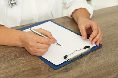 Doctor writing at wooden table, closeup view