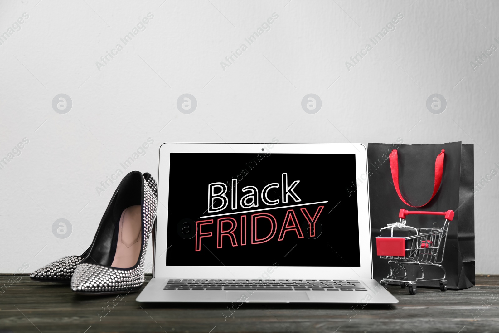 Photo of Composition with laptop and small shopping cart on wooden table against white background, space for text. Black Friday sale