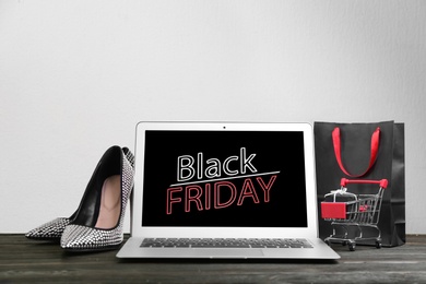 Photo of Composition with laptop and small shopping cart on wooden table against white background, space for text. Black Friday sale