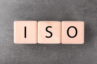 Photo of Wooden cubes with abbreviation ISO on grey textured table, flat lay