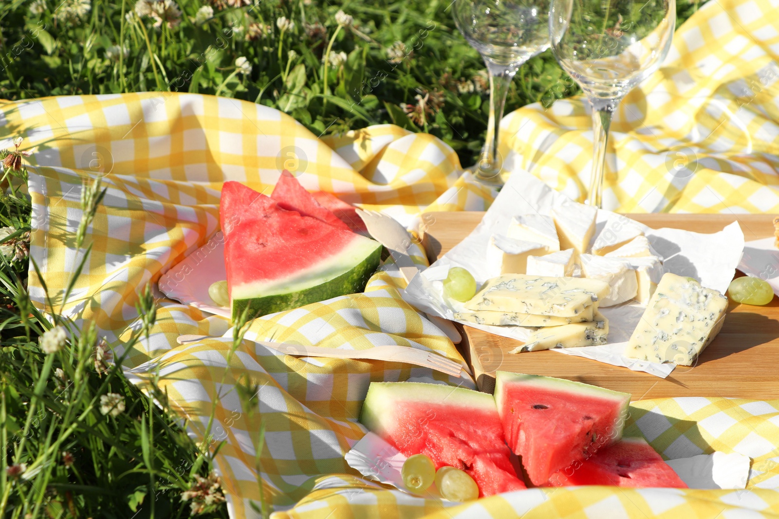 Photo of Picnic blanket with delicious food and wineglasses on green grass outdoors, closeup