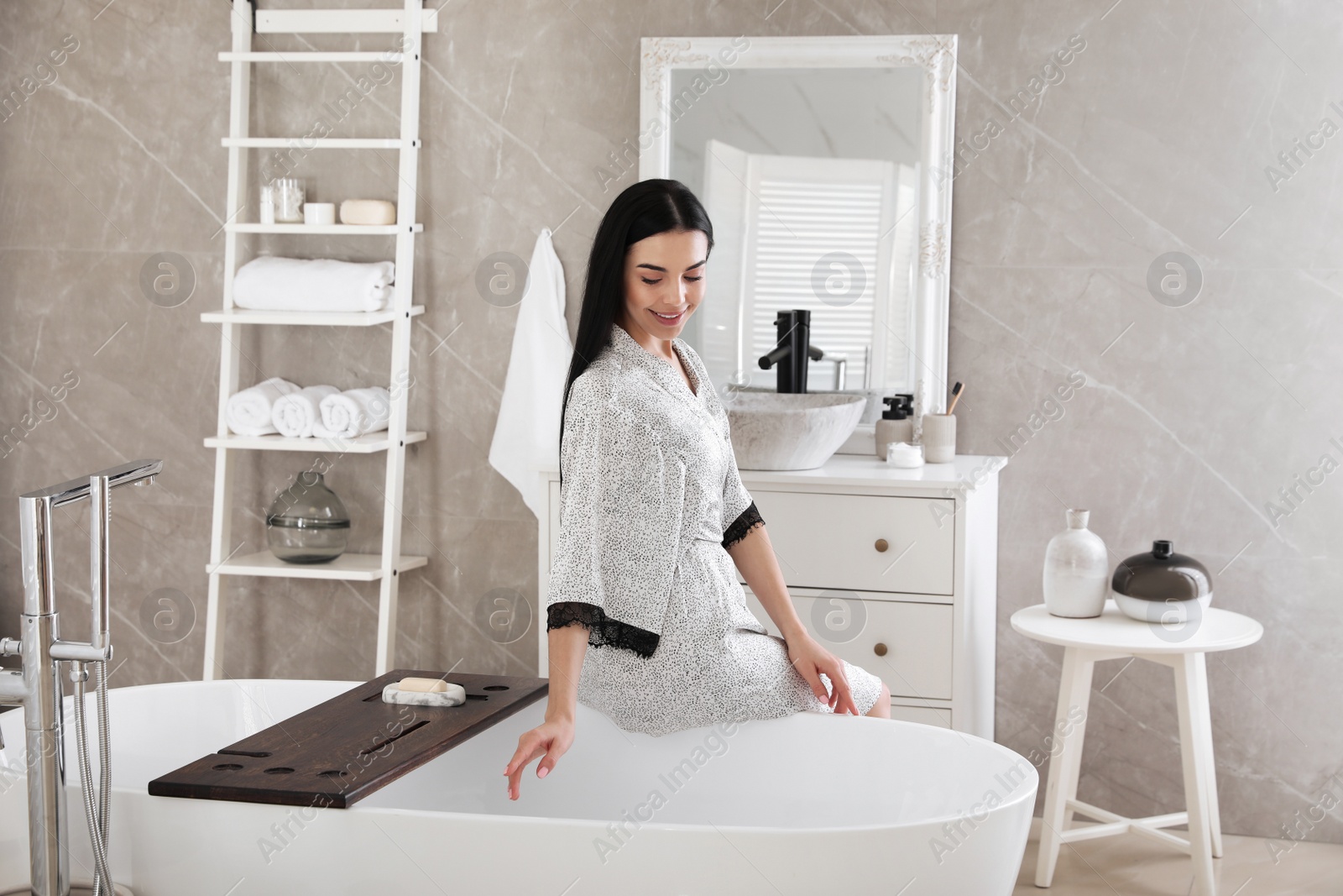 Photo of Beautiful young woman sitting on edge of tub in bathroom