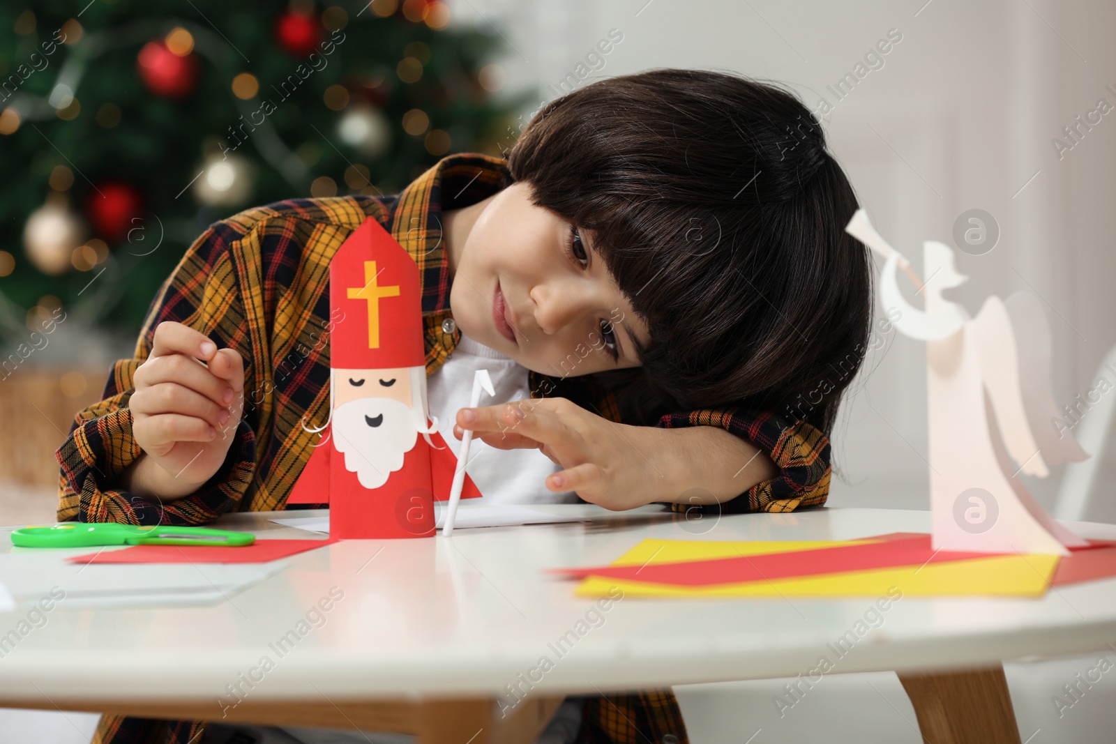 Photo of Cute little boy making paper Saint Nicholas toy at home