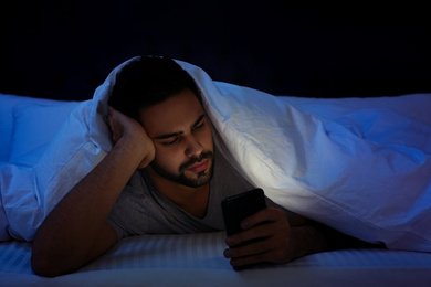 Photo of Young man addicted to smartphone in bed at night