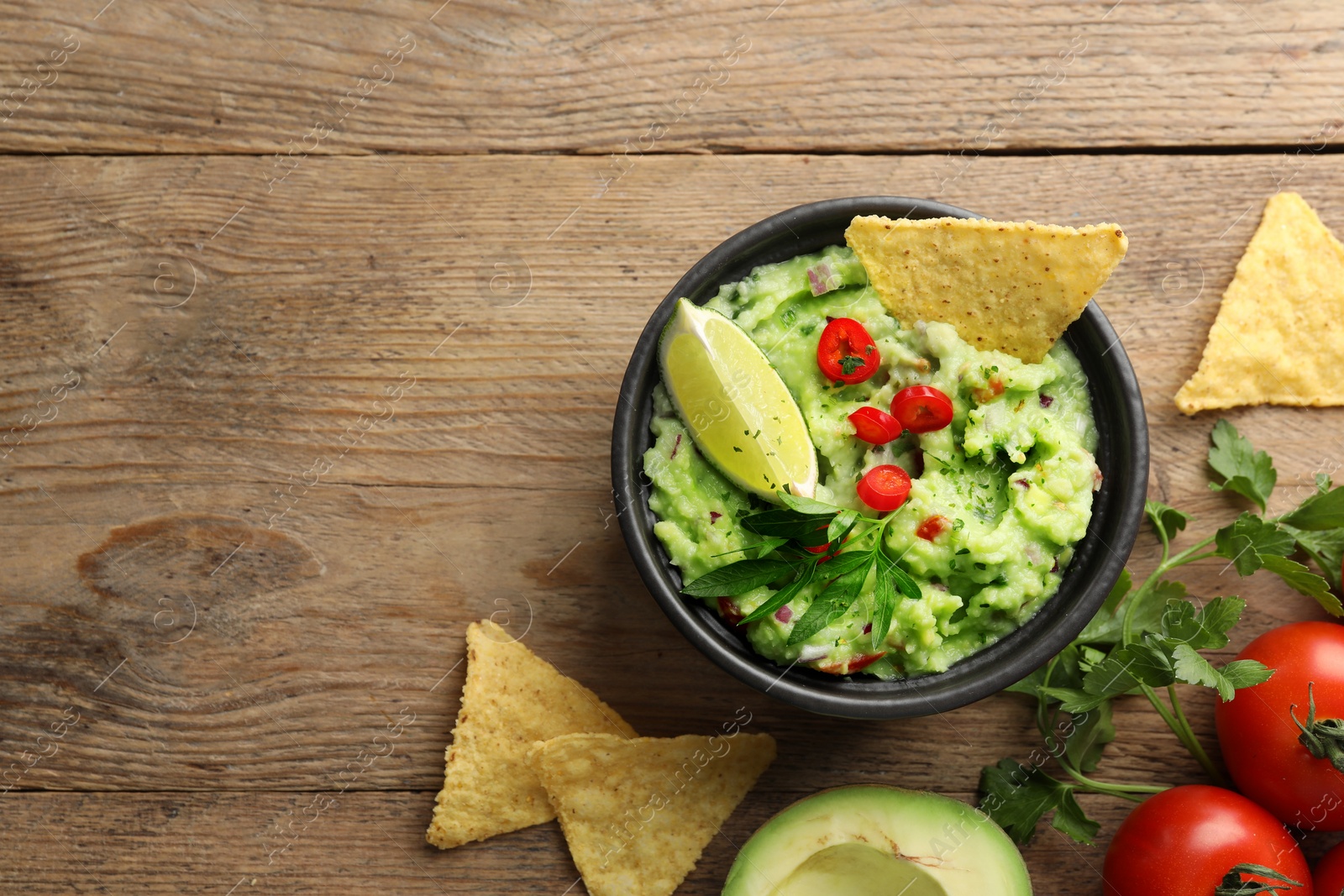 Photo of Delicious guacamole with nachos chips and ingredients on wooden table, flat lay. Space for text