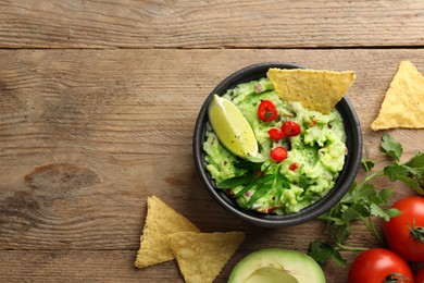 Delicious guacamole with nachos chips and ingredients on wooden table, flat lay. Space for text