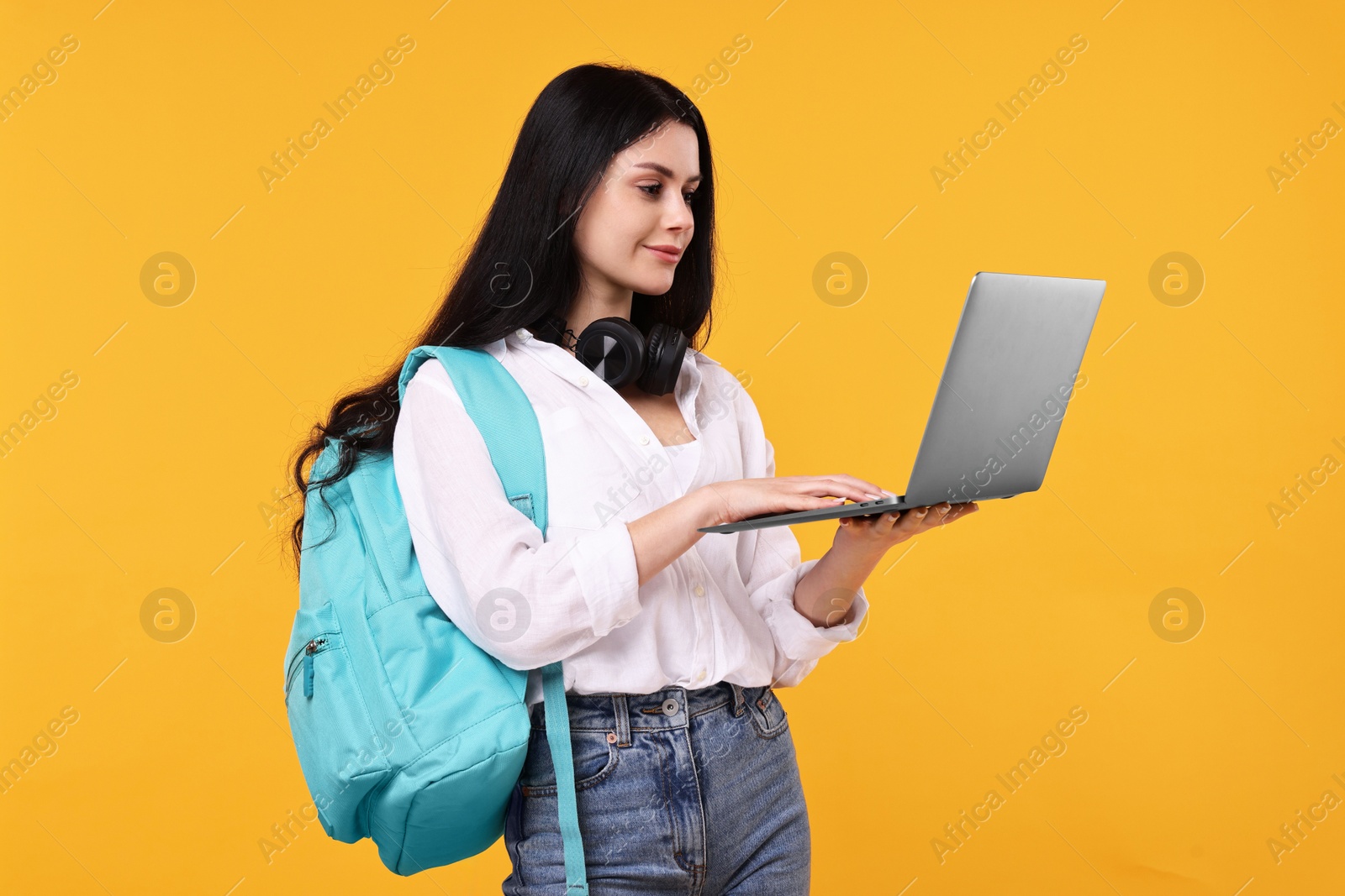 Photo of Student with laptop and backpack on yellow background