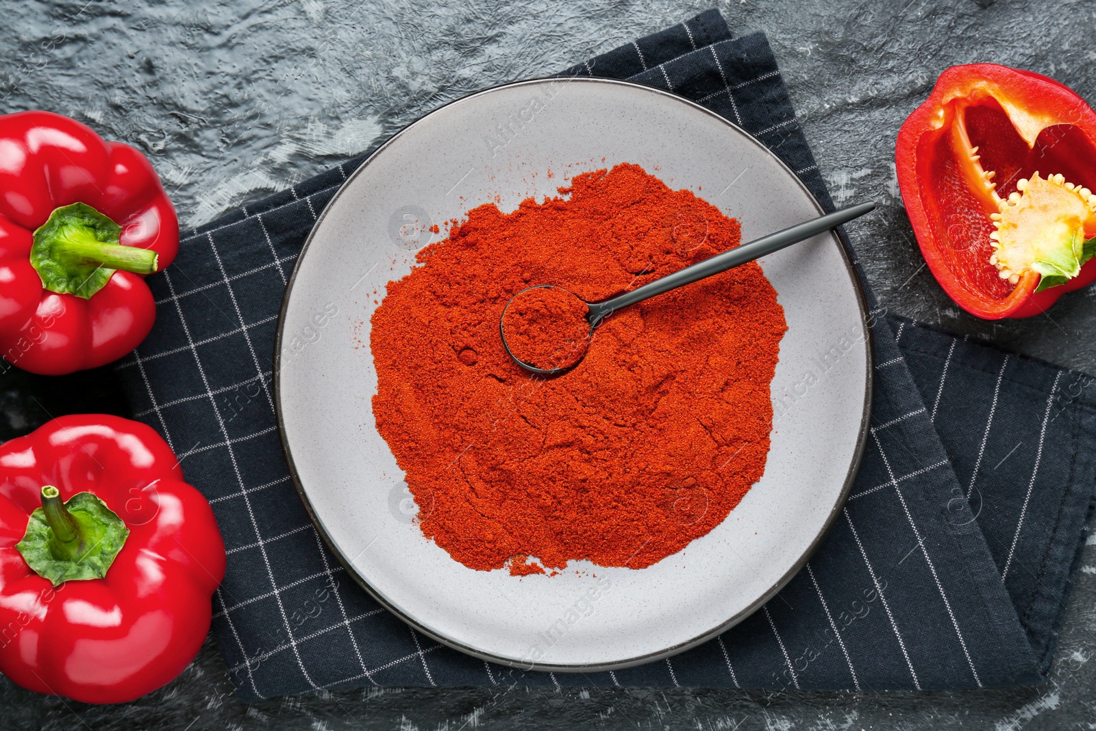 Photo of Plate of aromatic paprika and fresh peppers on black textured table, flat lay