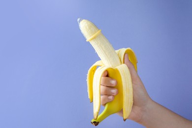 Photo of Woman holding banana in condom on light blue background, closeup and space for text. Safe sex concept