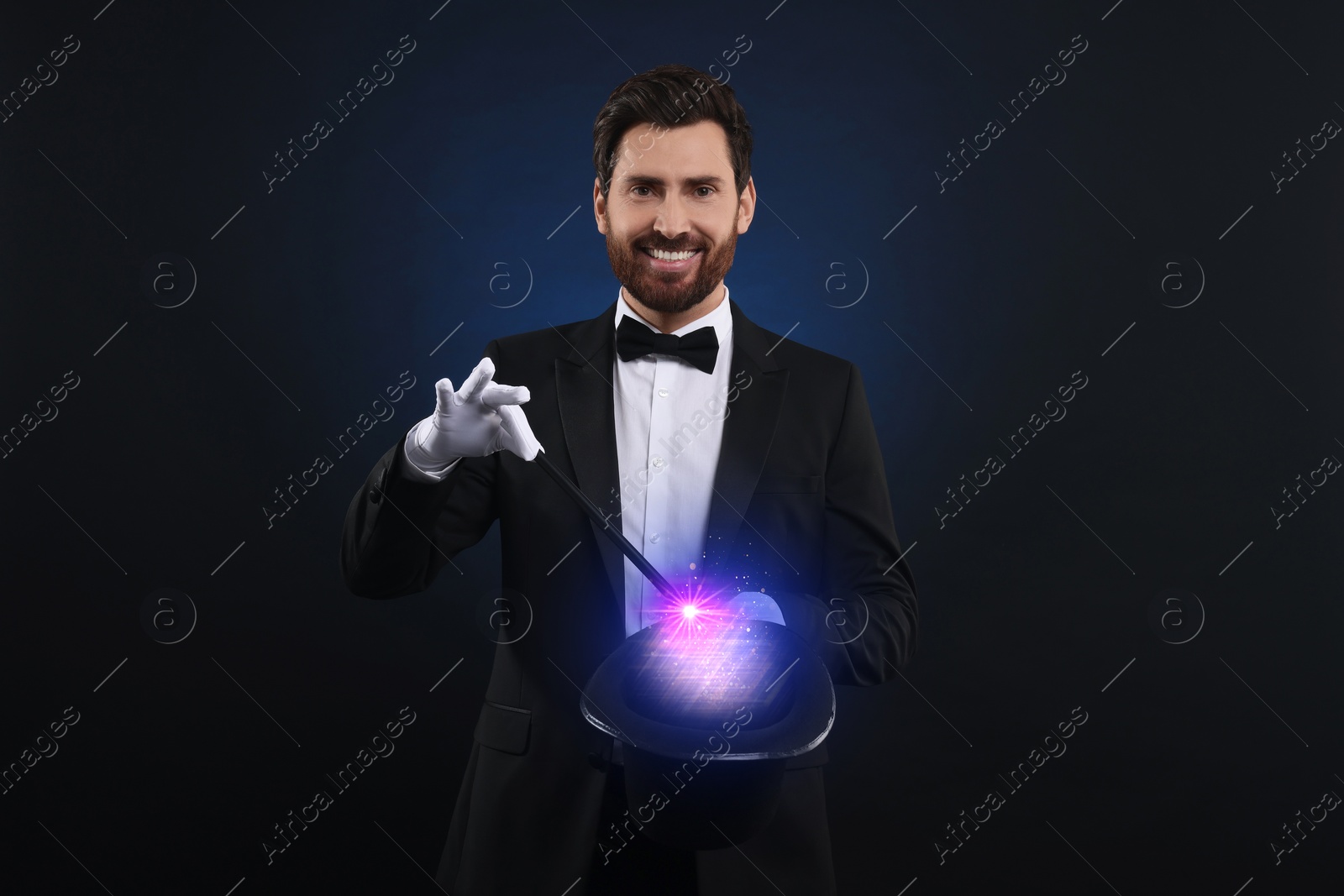 Image of Magician showing trick with wand and top hat on dark background. Fantastic light coming out of hat