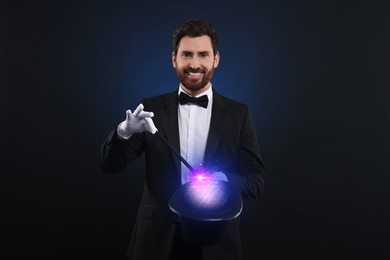 Image of Magician showing trick with wand and top hat on dark background. Fantastic light coming out of hat