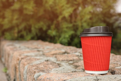 Cardboard coffee cup with lid on stone surface outdoors. Space for text